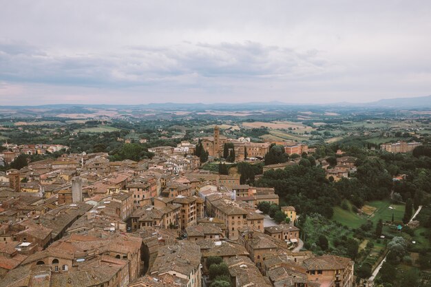 Panoramablick auf die Stadt Siena mit historischen Gebäuden und weit entfernten grünen Feldern von Torre del Mangia ist ein Turm in der Stadt. Sonniger Sommertag und dramatischer blauer Himmel