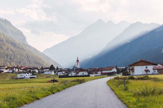 Foto panoramablick auf ein dorf in den österreichischen alpen von einer straße mit sonnenstreifen durch die berge