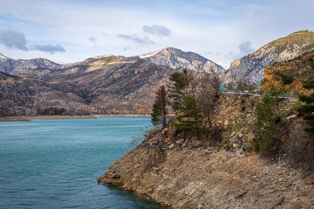 Panoramablick auf einen Bergsee mit klarem türkisgrünem Wasser vor dem Hintergrund einer Straße und eines Bauerndorfes