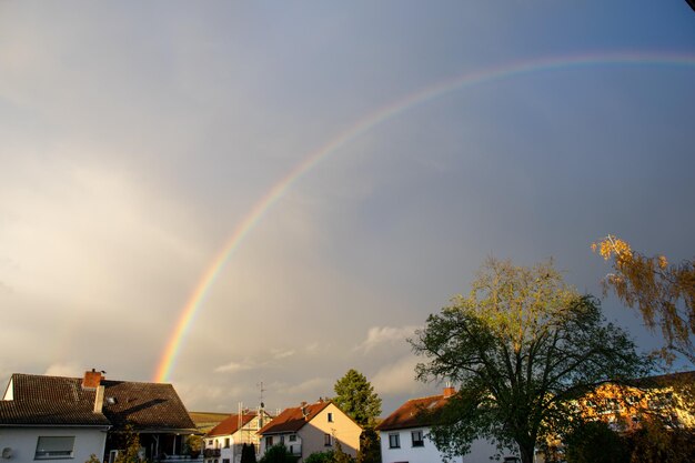 Panoramablick auf einen Regenbogen mit dunklen Wolken über den Häusern nach einem Regensturm