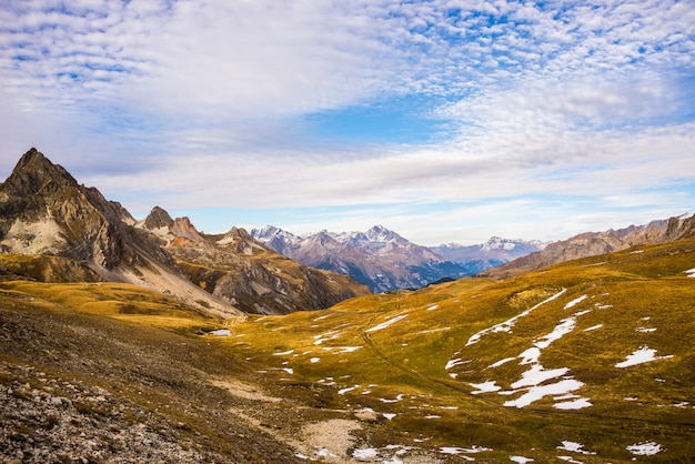 Panoramablick auf Tal und Gebirge in einem farbenfrohen Herbst mit gelben Wiesen und hohen Berggipfeln.