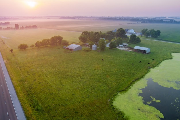 Panoramablick mit Sonnenaufgang auf einem Feld mit grünem Gras in der Nähe eines Teiches in einem kleinen Dorf