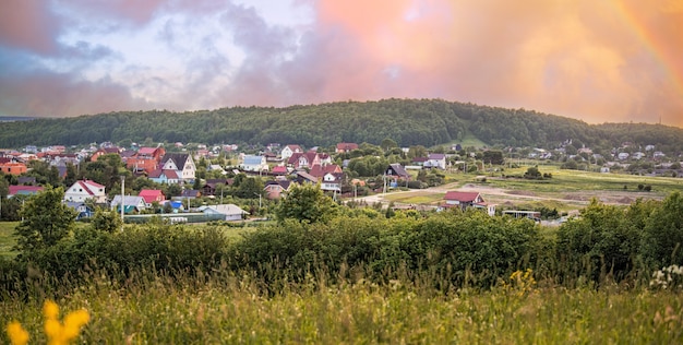 Panoramablick vom Berg auf eine kleine ländliche Siedlung zwischen Feldern und Wäldern bei Sonnenuntergang im Sommer.