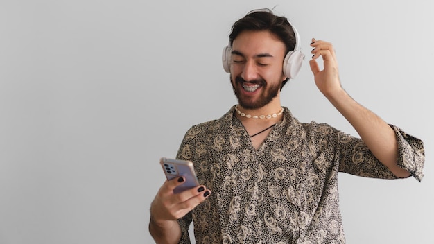 Panoramafoto eines jungen schwulen lateinischen Queer-Mannes, der mit seinen drahtlosen Kopfhörern Musik von seinem Handy hört Kopieren Sie Platz