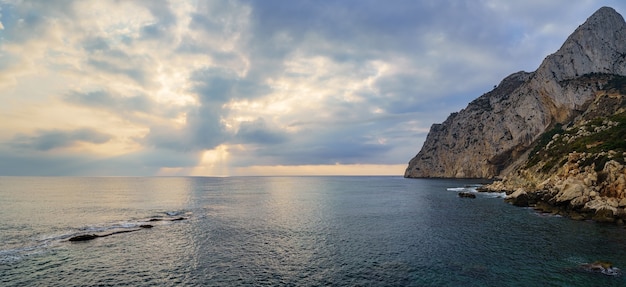 Panoramameerblick mit großem Berg am Meer und goldenem Sonnenuntergang.