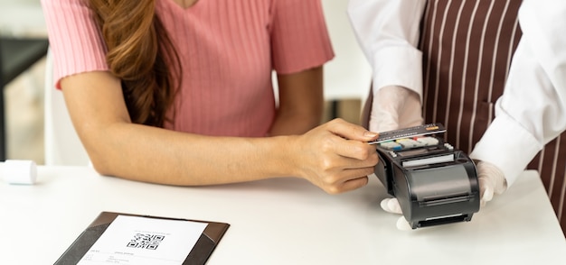 Panoramic Close up Cliente mujer asiática realiza pago con tarjeta de crédito sin contacto después de comer en un nuevo restaurante a distancia social normal para reducir el contacto. Concepto de tecnología y sin contacto en línea.