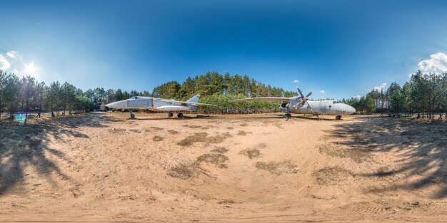 Panorámica hdri esférica completa Vista de ángulo de 360 grados en campamento de guerrilla forestal con viejos aviones de transporte militar y aviones de combate en bosque de pinos en proyección equirectangular Contenido VR AR