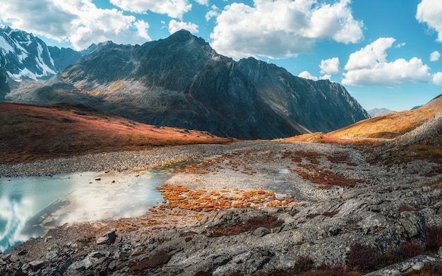 Panorámico paisaje alpino con hermoso lago de montaña con arroyos en el valle de las tierras altas de altas montañas bajo un cielo nublado azul. Paisaje de montaña soleado con lago glaciar espejo en alta montaña.