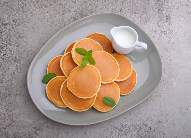 Panqueca em um prato com morangos decorados com hortelã em uma mesa de concreto