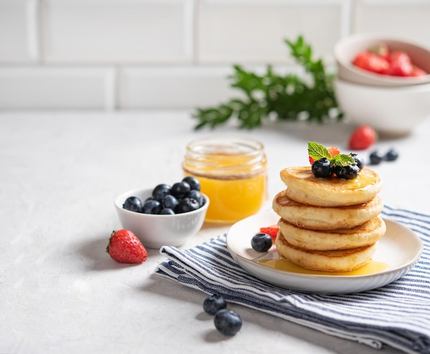 Panquecas americanas clássicas caseiras em uma pilha com frutas frescas e mel em um guardanapo listrado em um fundo de tijolo branco embaçado. O conceito de um pequeno-almoço saudável e dietético. Espaço para texto.