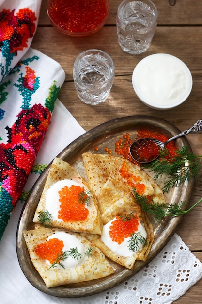 Panquecas caseiras com caviar vermelho, creme de leite e endro, servidos com vodka. Estilo rústico.