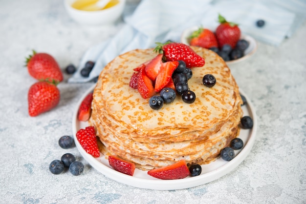 Panquecas caseiras finas em um prato com frutas frescas e mel.