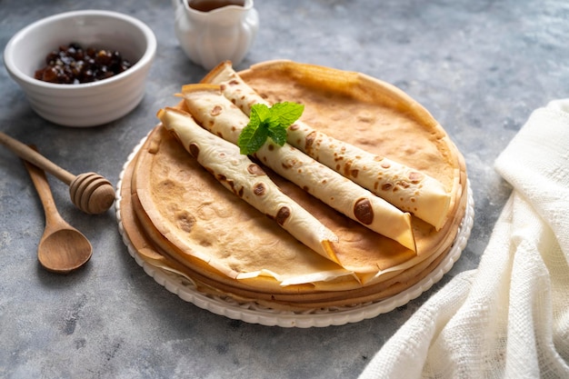 Panquecas caseiras ou crepes com geléia e mel, em fundo cinza.