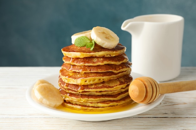 Panquecas com banana e mel na mesa de madeira branca