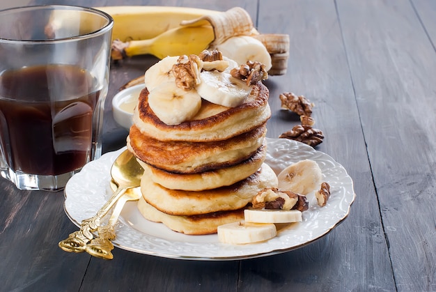 Panquecas com banana, nozes, mel e xícara de café em fundo escuro