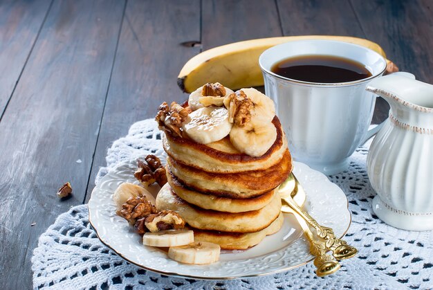 Panquecas com banana, nozes, mel e xícara de café em fundo escuro