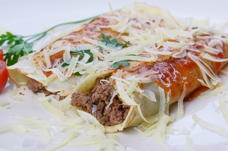 Foto panquecas com carne, ao molho de tomate e queijo, com coentro e queijo ralado por cima.