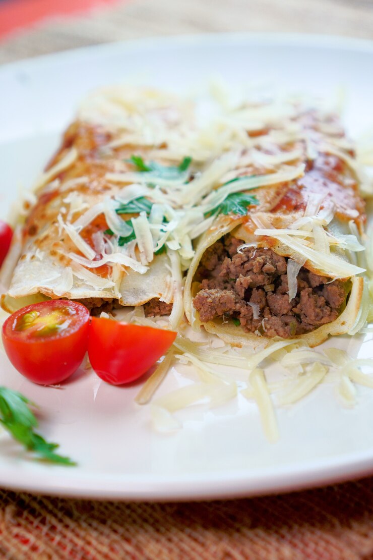 Foto panquecas com carne, ao molho de tomate e queijo, com coentro e queijo ralado por cima.
