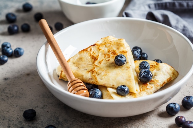 Panquecas com frutas e mel em um prato branco.