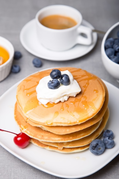 Panquecas com mirtilos, cerejas, creme de leite, mel e café. Fechar-se. Foco seletivo.