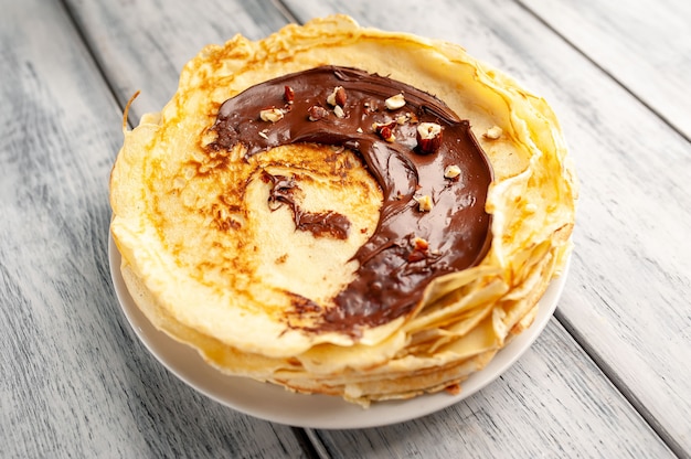 Panquecas com pasta de chocolate e avelãs, num prato branco na madeira