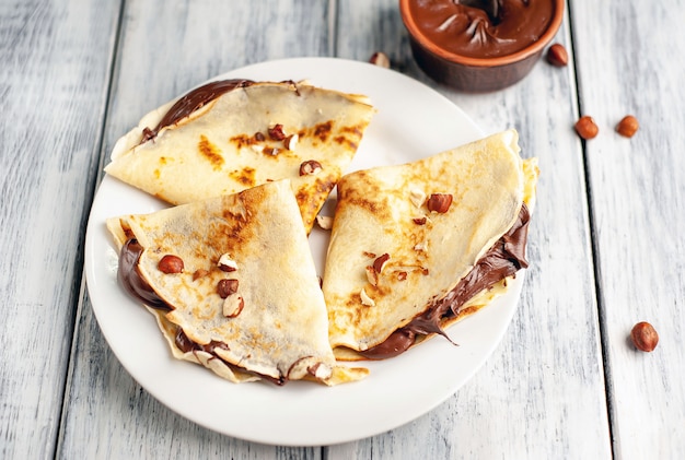 Panquecas com propagação de chocolate e avelãs, num prato branco sobre um fundo de madeira