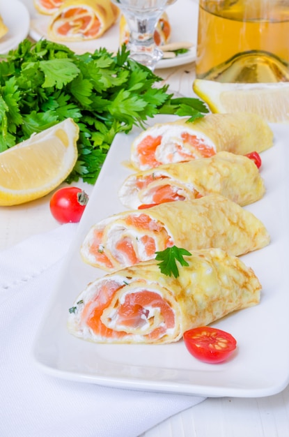 Panquecas (crepes) com salmão defumado, cream cheese e ervas na superfície de madeira branca