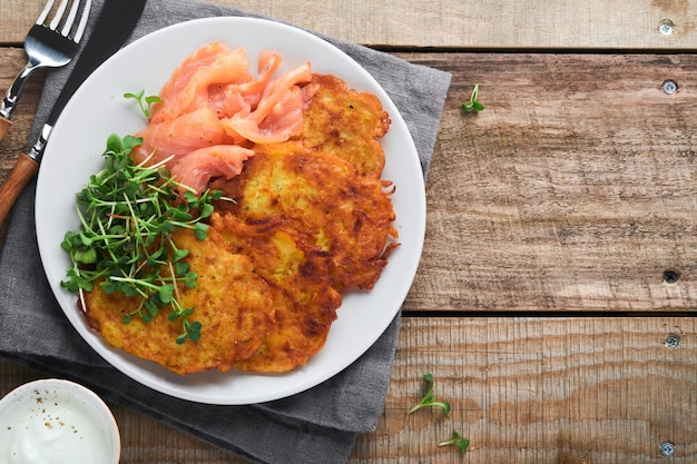 Panquecas de batata Panquecas de batata caseira frita ou latkes com creme de cebola verde microgreens salmão vermelho e molho em prato rústico no fundo da mesa de madeira velha Estilo rústico Vista superior