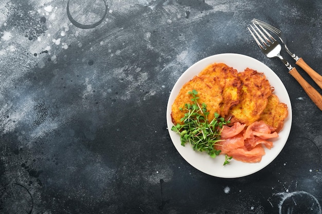 Panquecas de batata Panquecas de batata caseira frita ou latkes com creme de cebola verde microgreens salmão vermelho e molho em prato rústico no fundo da mesa preta velha Estilo rústico Vista superior