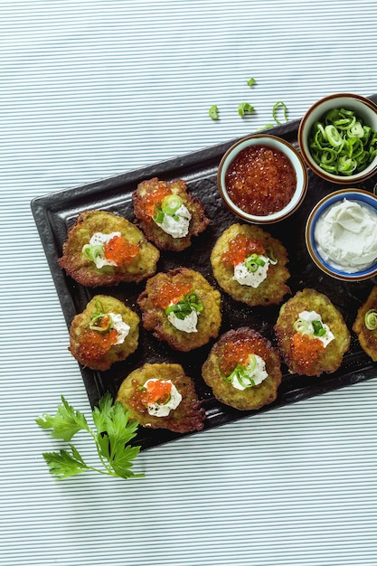 Panquecas de batata tradicionais russas servidas com caviar vermelho, cebola verde e creme de leite em uma bandeja com vinho branco e limão