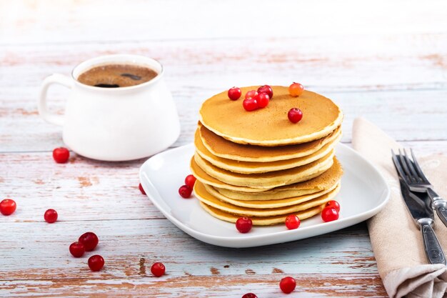 Panquecas de café da manhã com cranberries em uma mesa de madeira e uma xícara de café.