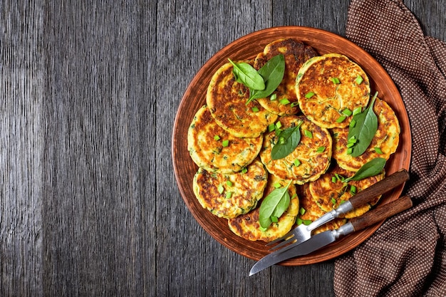 Panquecas de espinafre de grão de bico em um prato de barro em uma mesa de madeira escura com hummus em uma tigela pequena, plana, espaço livre