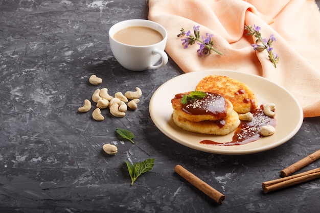 Panquecas de queijo com molho de caramelo em uma placa de cerâmica bege e uma xícara de café em concreto preto