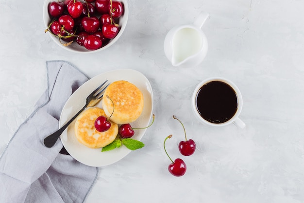 Panquecas de queijo cottage com cereja berry, xícara de café preto, leite e tigela