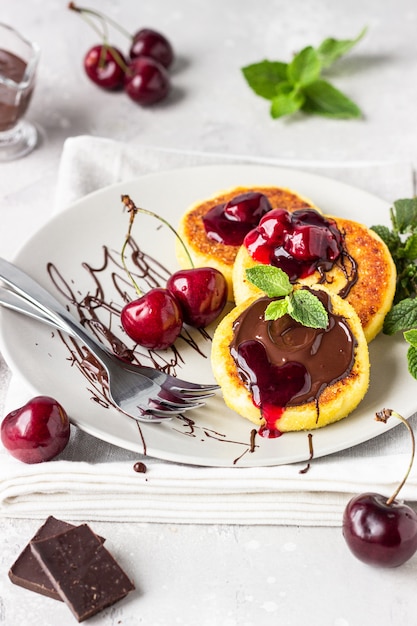 Panquecas de queijo cottage com geléia de chocolate e cereja, cereja fresca e hortelã. Cozinha tradicional ucraniana e russa. Syrniki. Café da manhã saudável e dieta.