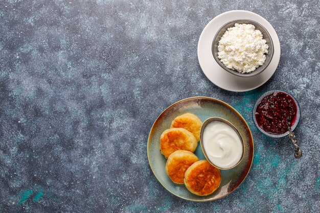 Panquecas de queijo cottage com geléia de framboesa. sirniki russo ou sirniki, bolinhos de queijo cottage ou panquecas com uma tigela de queijo fresco caseiro em cinza escuro