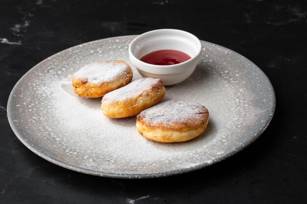 Panquecas de queijo cottage Syrniki ou Cheesecakes com molho vermelho isolado em fundo de mármore preto Comida caseira Café da manhã saboroso Foco seletivo