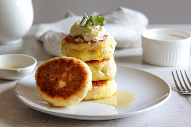 Panquecas de queijo doce com mel e creme em um prato branco Cheesecakes de receita caseira