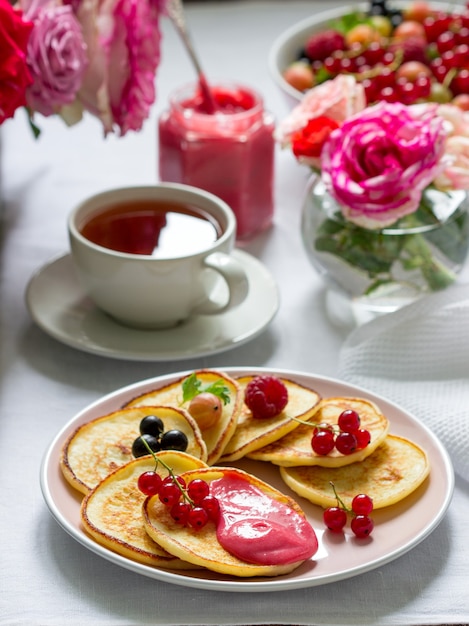 Panquecas de requeijão com requeijão de amoras servidas com chá em uma mesa decorada com buquês de rosas.