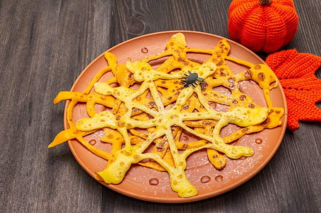 Panquecas de teia de aranha com calda de açúcar e pó no café da manhã de halloween. com crochê laranja abóbora e folha