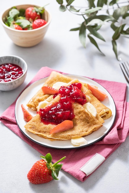 Foto panquecas doces com morangos frescos e banana sobre um fundo claro o conceito de comida caseira