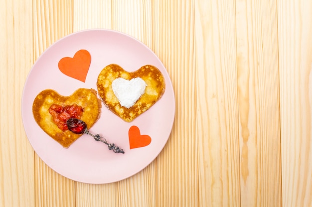 Foto panquecas em forma de coração para café da manhã romântico com geléia de morango, colher de prata e corações de papel