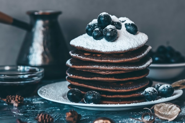 Panquecas em um prato branco em açúcar em pó com uvas em um fundo cinza