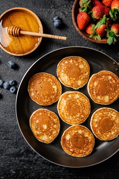 Panquecas em uma frigideira com frutas frescas e mel