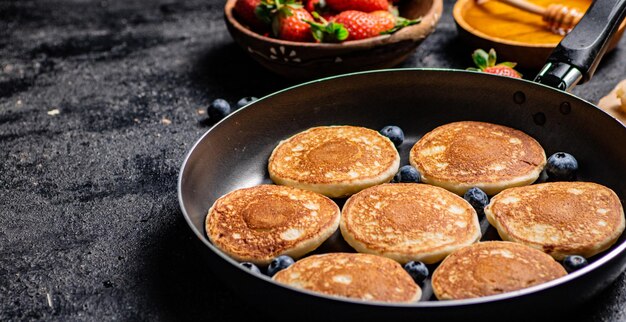 Foto panquecas em uma frigideira com frutas frescas e mel