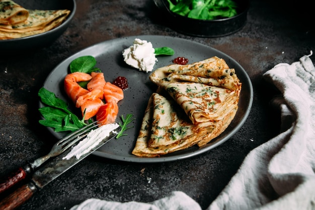 Panquecas finas com ervas, salmão e cream cheese em um prato