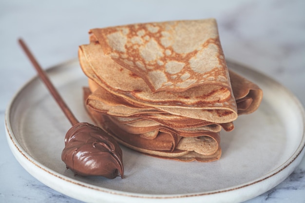 Panquecas finas doces tradicionais com uma colher de creme de chocolate