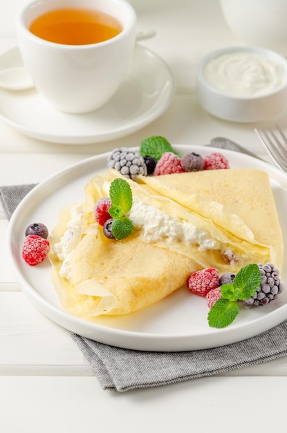 Panquecas finas ou crepes com queijo cottage e passas com frutas vermelhas, mel e creme de leite