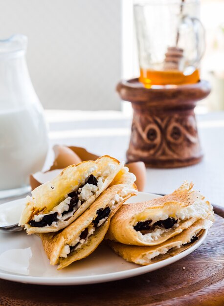 Panquecas finas recheadas com queijo, ameixas e creme de leite, leite, café da manhã, em uma tábua de madeira