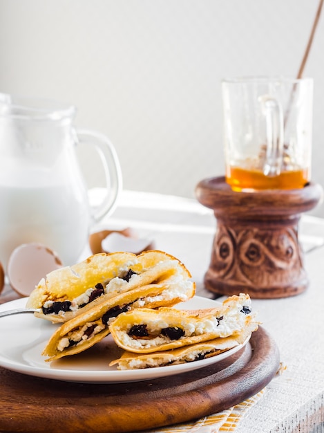 Panquecas finas recheadas com queijo, ameixas e creme de leite, leite, café da manhã, em uma tábua de madeira